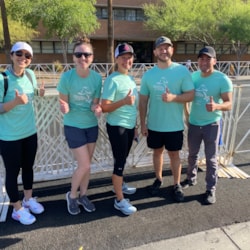Five volunteers smile and give thumbs up at finish line of 5K event